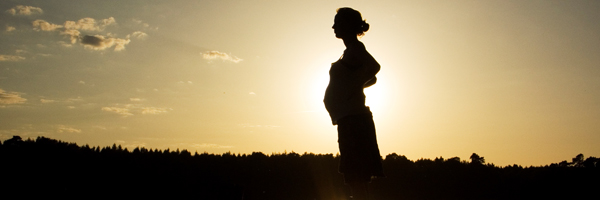 Schwangere Frau vor Sonnenaufgang